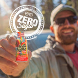 A man in sunglasses and a cap holds up a small bottle of Fruity Rainbow 5-hour Energy candy in the Taste Caffeine flavor. A large circular graphic overlay reading 'Zero Sugar' is superimposed over the top left.
