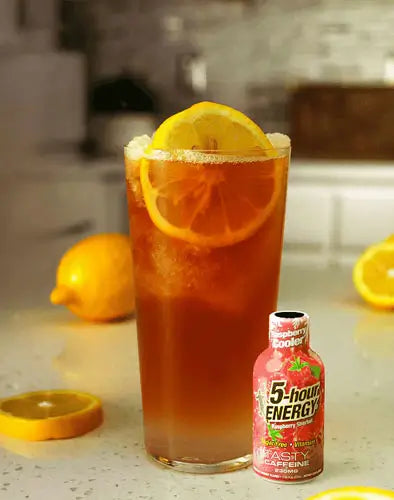 A tall glass of iced tea with a lemon slice garnish sits on a kitchen counter next to a small bottle of 5-hour Energy Raspberry Cooler.