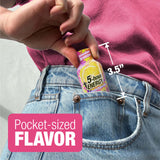 A close-up of a person's hand holding a small 'Pocket-sized 5-hour ENERGY'  The person is wearing a pink top and light blue denim jeans