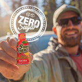 A man outdoors holds up a bottle of 5-hour Energy Extra Strength Zero Sugar. A large circular graphic overlay reading 'ZERO Sugar' is superimposed over the top of the image.