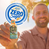 A man in a pink shirt holds up a bottle of Tidal Twist 5-hour Energy bottle with a large blue 'Zero Sugar' graphic overlay in the foreground and a blurred beach background.