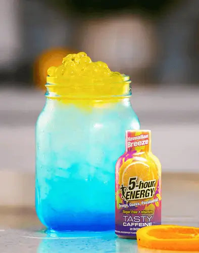 A blue and yellow layered drink in a clear mason jar with a yellow frothy top, shown next to a bottle of Hawaiian Breeze 5-hour Energy. 