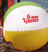 Beach ball with 5-hour ENERGY logo on a sandy surface next to a bottle of 5-hour ENERGY drink.