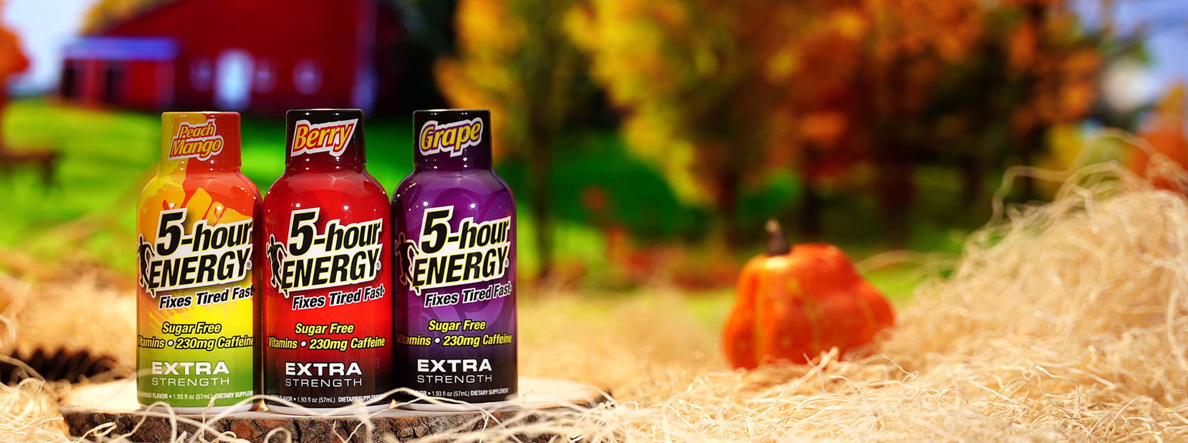 Three 5-hour Energy drinks in different flavors on a hay bale with a barn and pumpkins in the background.
