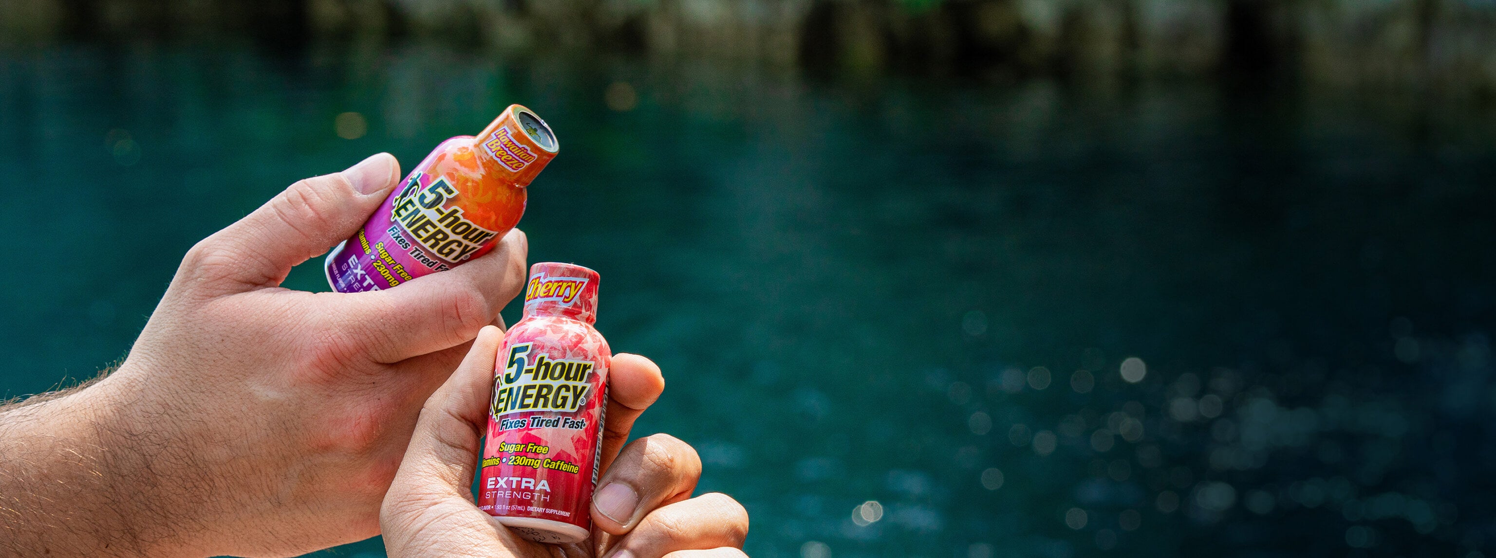 Two energy drink bottles held by a hand with a blurred natural background