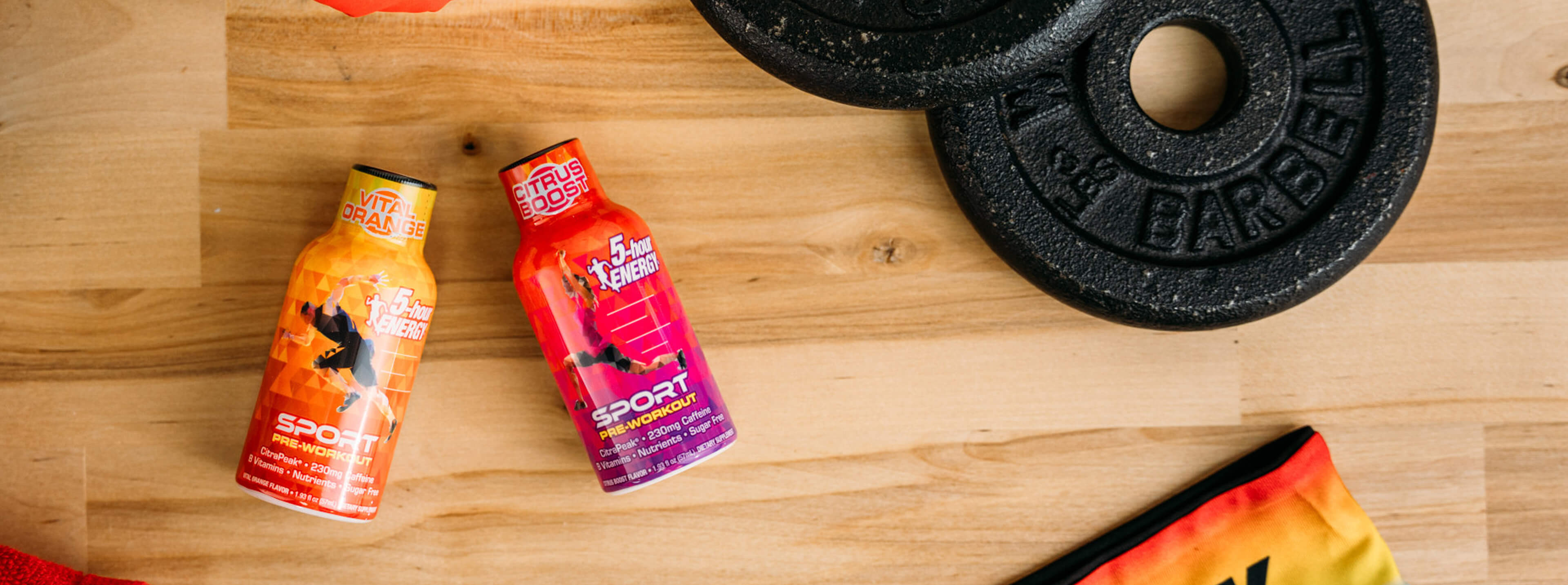 Two energy drink bottles on a wooden surface with a weight plate in the background.